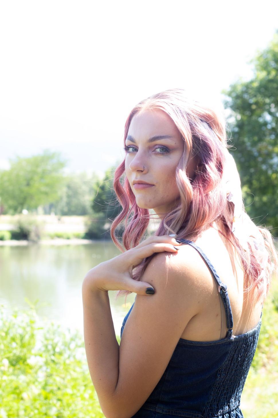 Free Image of Woman with wavy dyed hair posing near a tranquil lake 