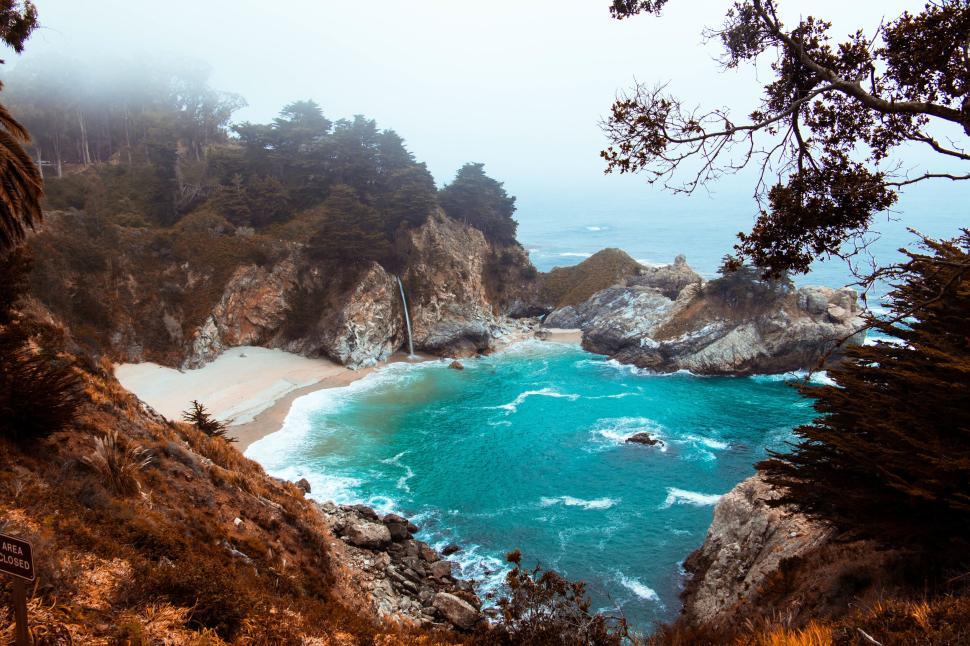 Free Image of Scenic beach cove with waterfall and turquoise waters. 