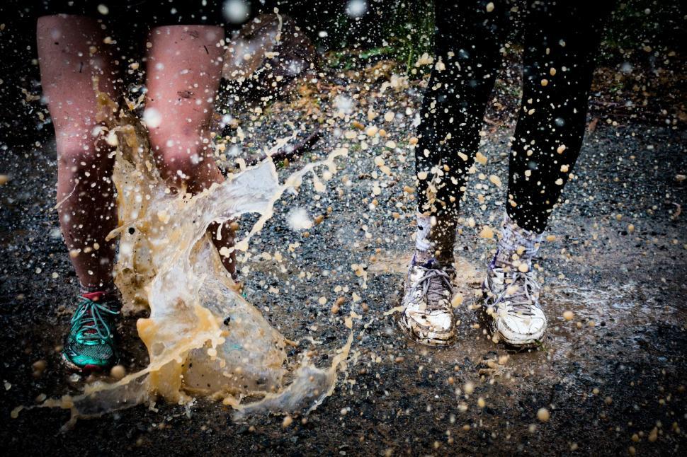 Free Image of Two people splashing through a muddy puddle outdoors. 