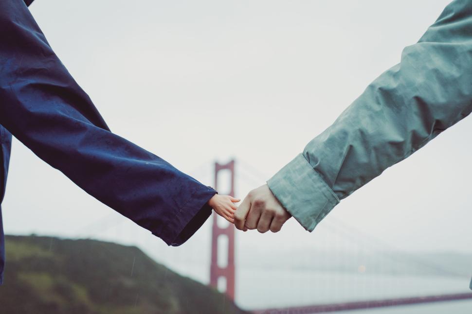 Free Image of Two people holding hands with iconic bridge in background. 