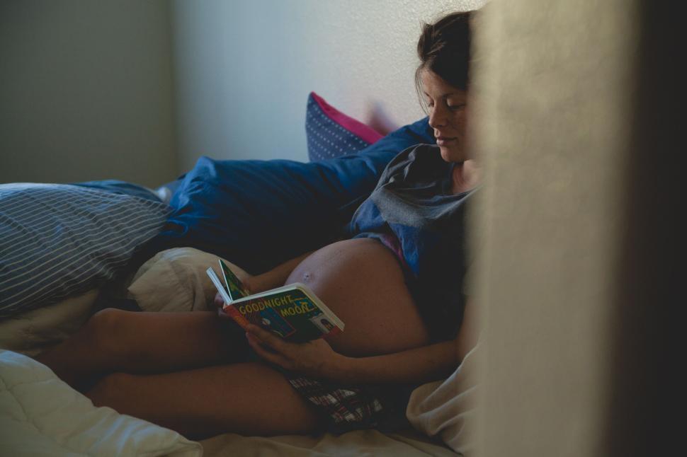 Free Image of Pregnant woman reads book while lying on cozy bed 