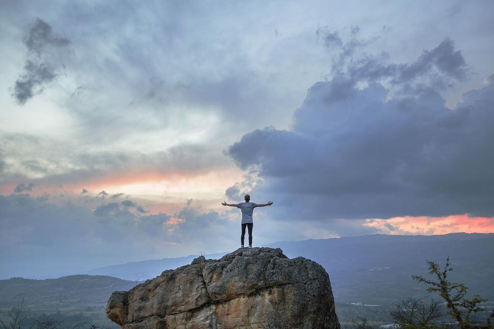 Free Image of Person on rock outcrop with arms wide open to sky. 
