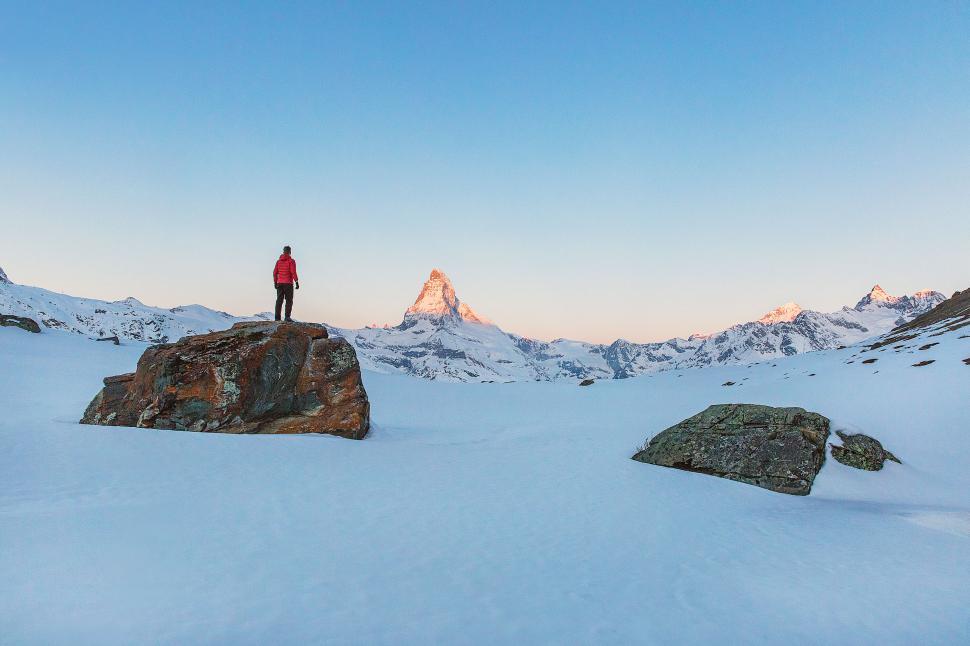 Free Image of Person in red jacket on snow near mountain at sunset. 