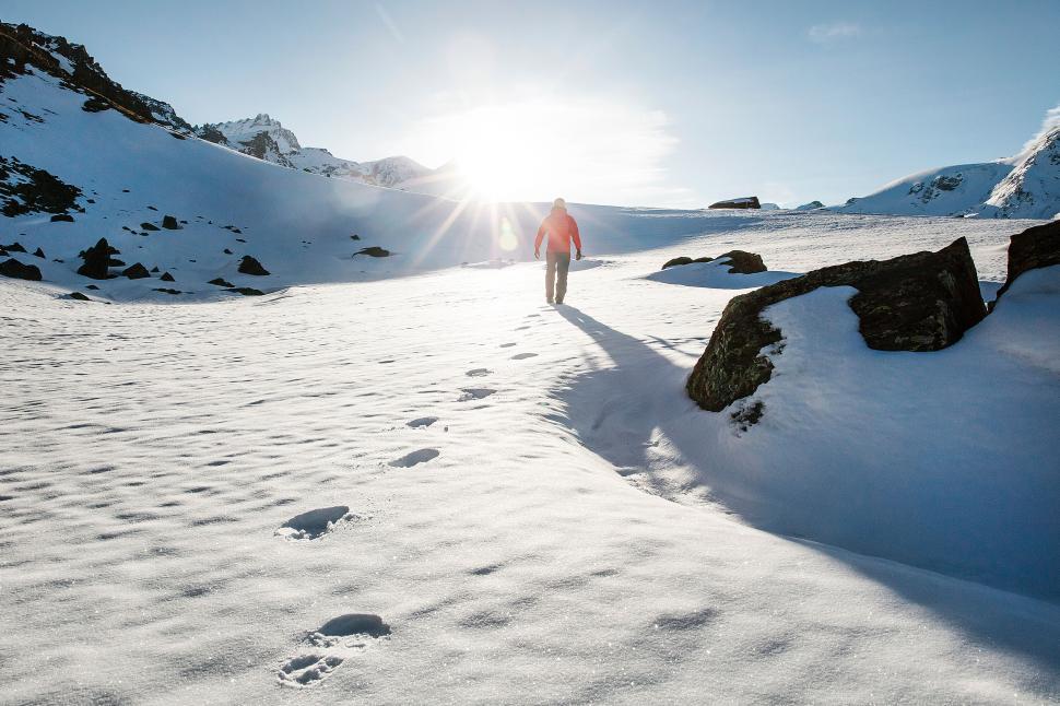 Free Image of Solo hiker leaving footprint trail in snowy terrain. 