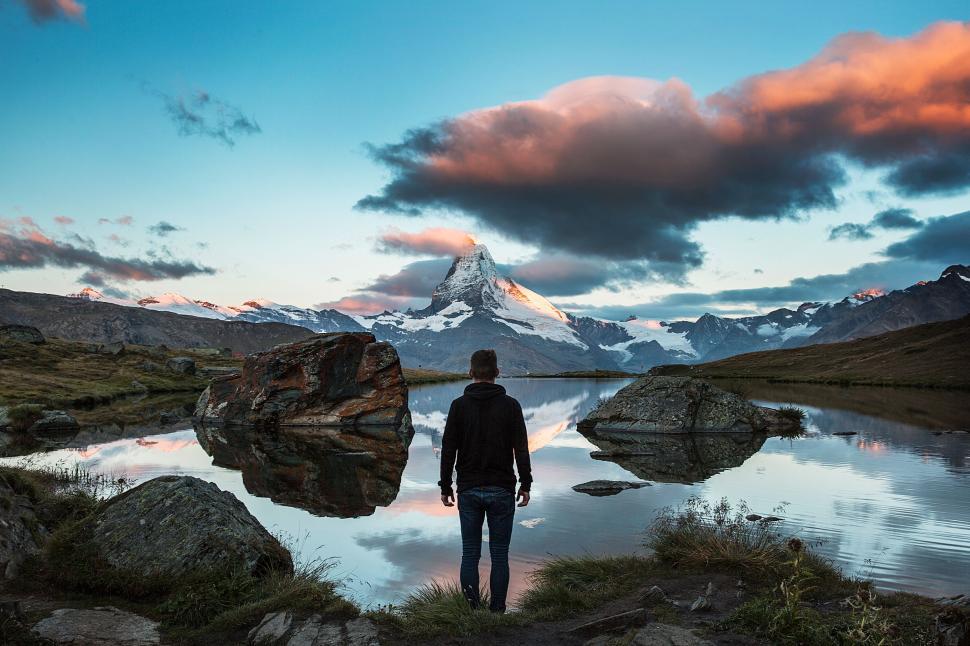 Free Image of Person stands at alpine lake with reflecting mountains. 