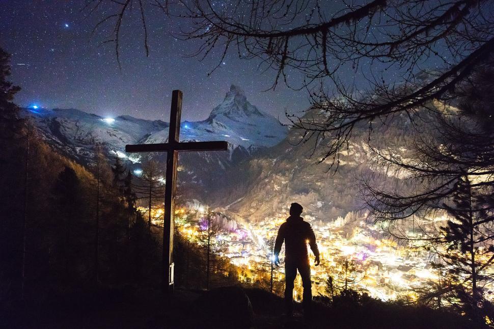 Free Image of Silhouette of man near cross overlooking lit town 