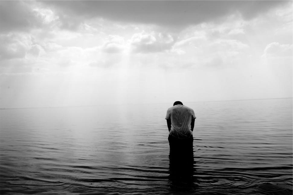 Free Image of Person standing in water under a cloudy sky at sunset. 