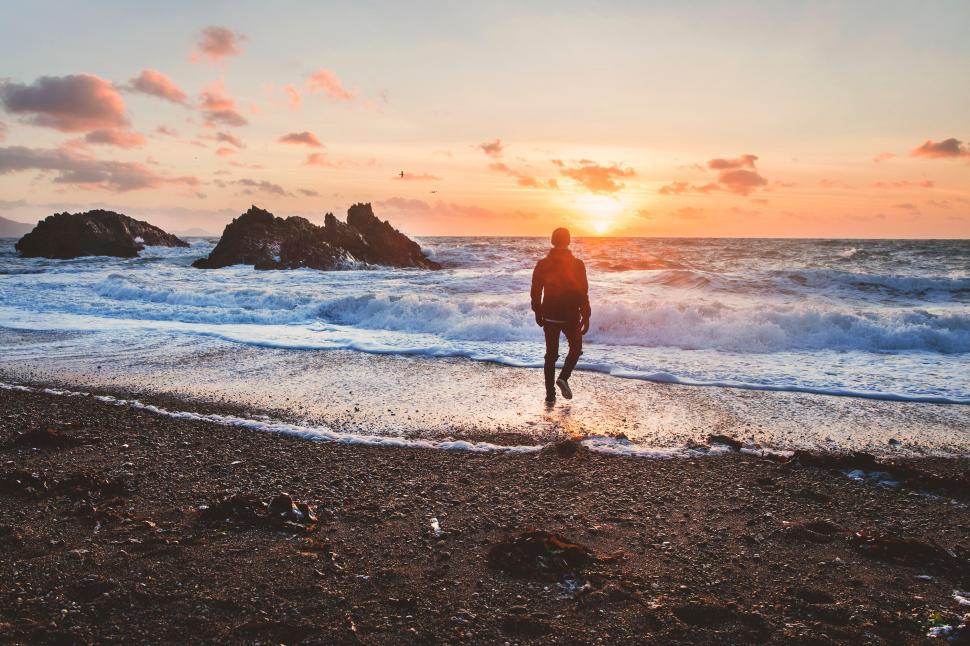 Free Image of Person walking on a beach at sunset towards the water. 