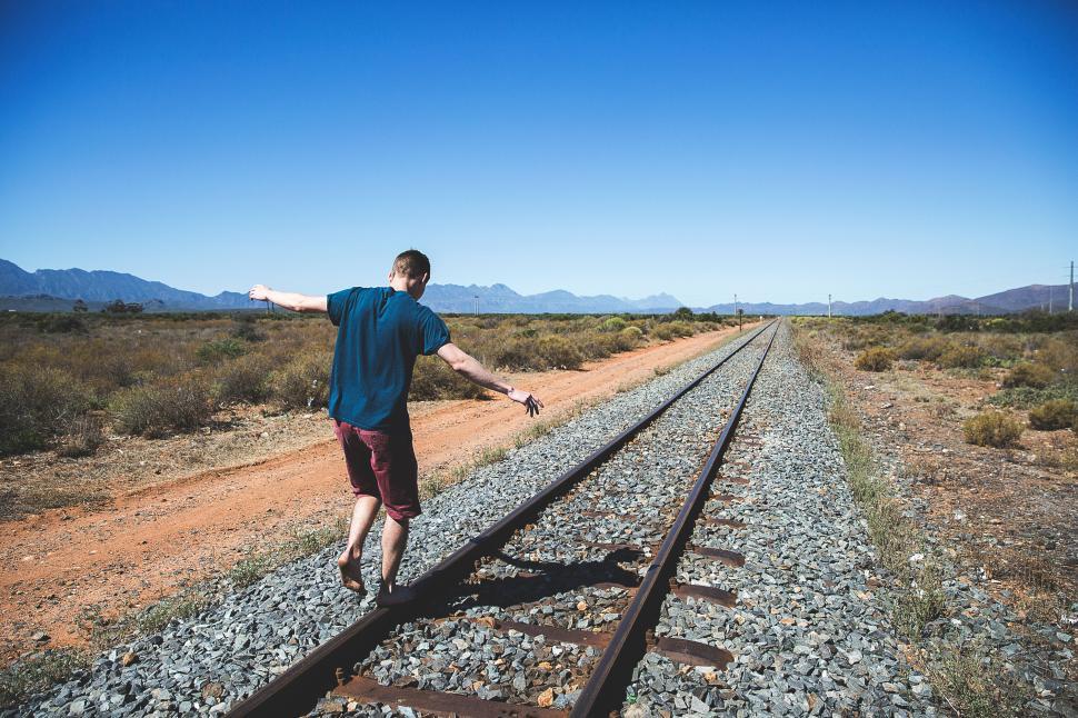 Free Image of Person balancing on rail tracks under a clear sky. 