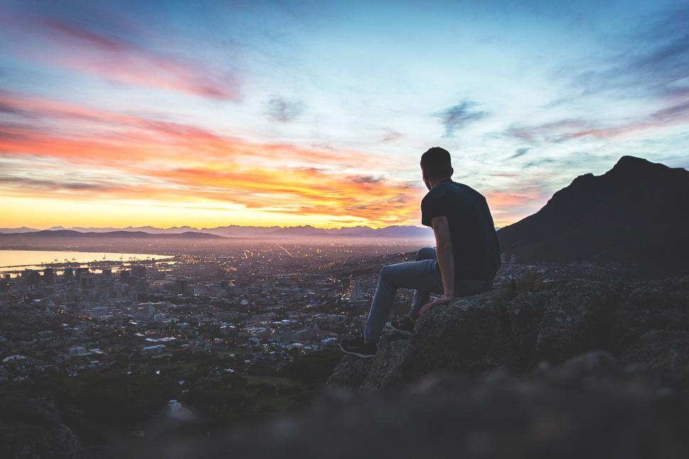Free Image of Silhouette of man on cliff overlooking city at sunset 