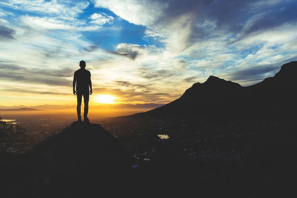 Free Image of Silhouetted man stands on peak watching golden sunrise 