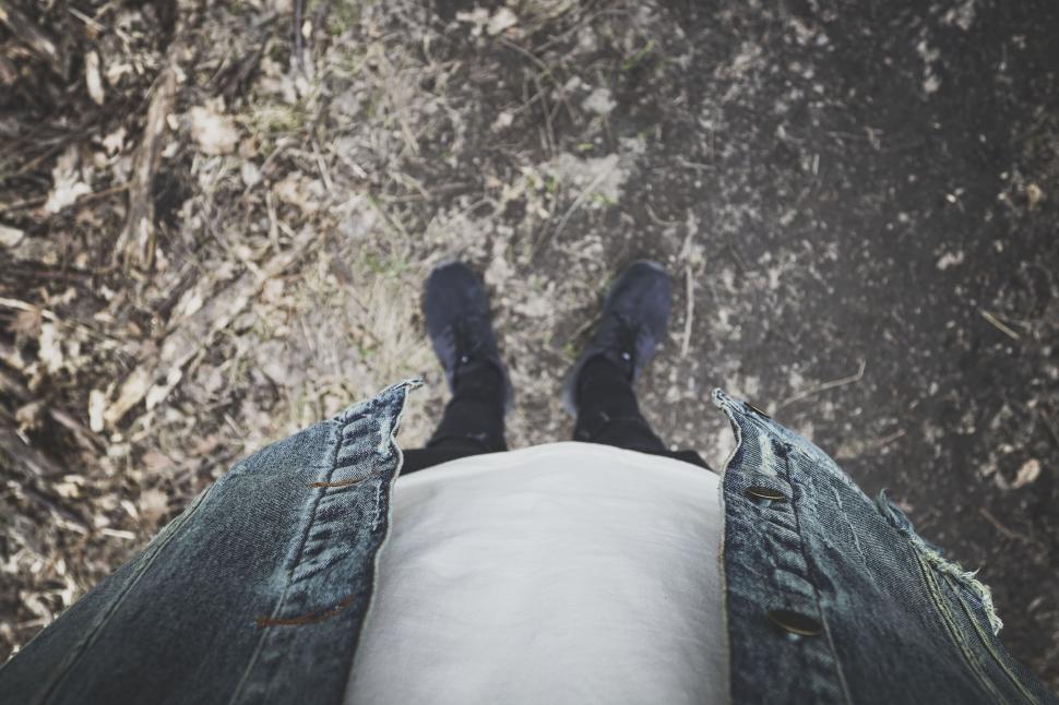 Free Image of Point of view shot looking down at worn jeans and dark sneakers. 