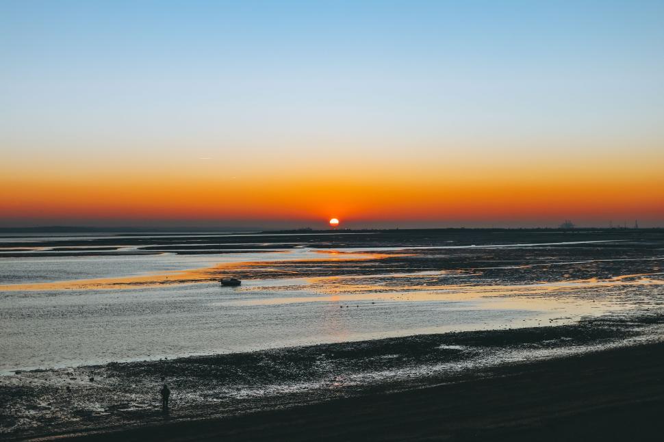 Free Image of Vibrant sunset over a calm bay with a boat on the horizon 