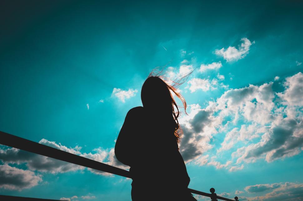 Free Image of Silhouette of a person against a bright blue cloudy sky 