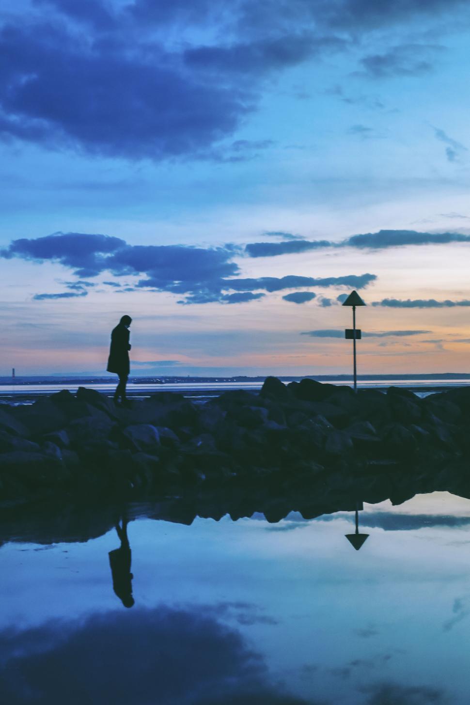 Free Image of Reflective silhouette of a person standing by the water at twilight 