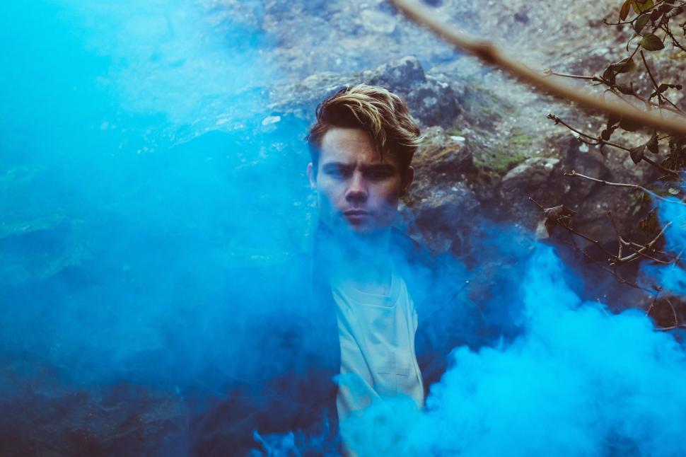 Free Image of Person stands in a foggy natural environment surrounded by blue smoke. 