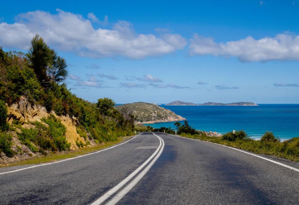 Free Image of Long road leading down to the sea with clear blue skies above. 