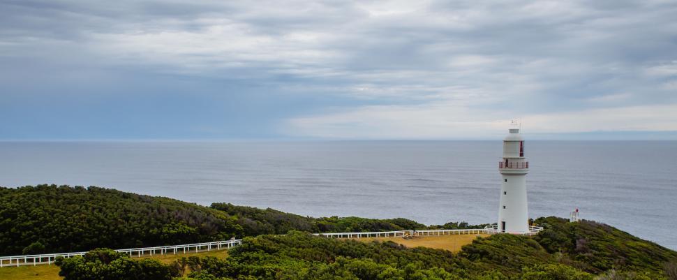 Free Image of White lighthouse standing on a cliff overlooking the open sea. 