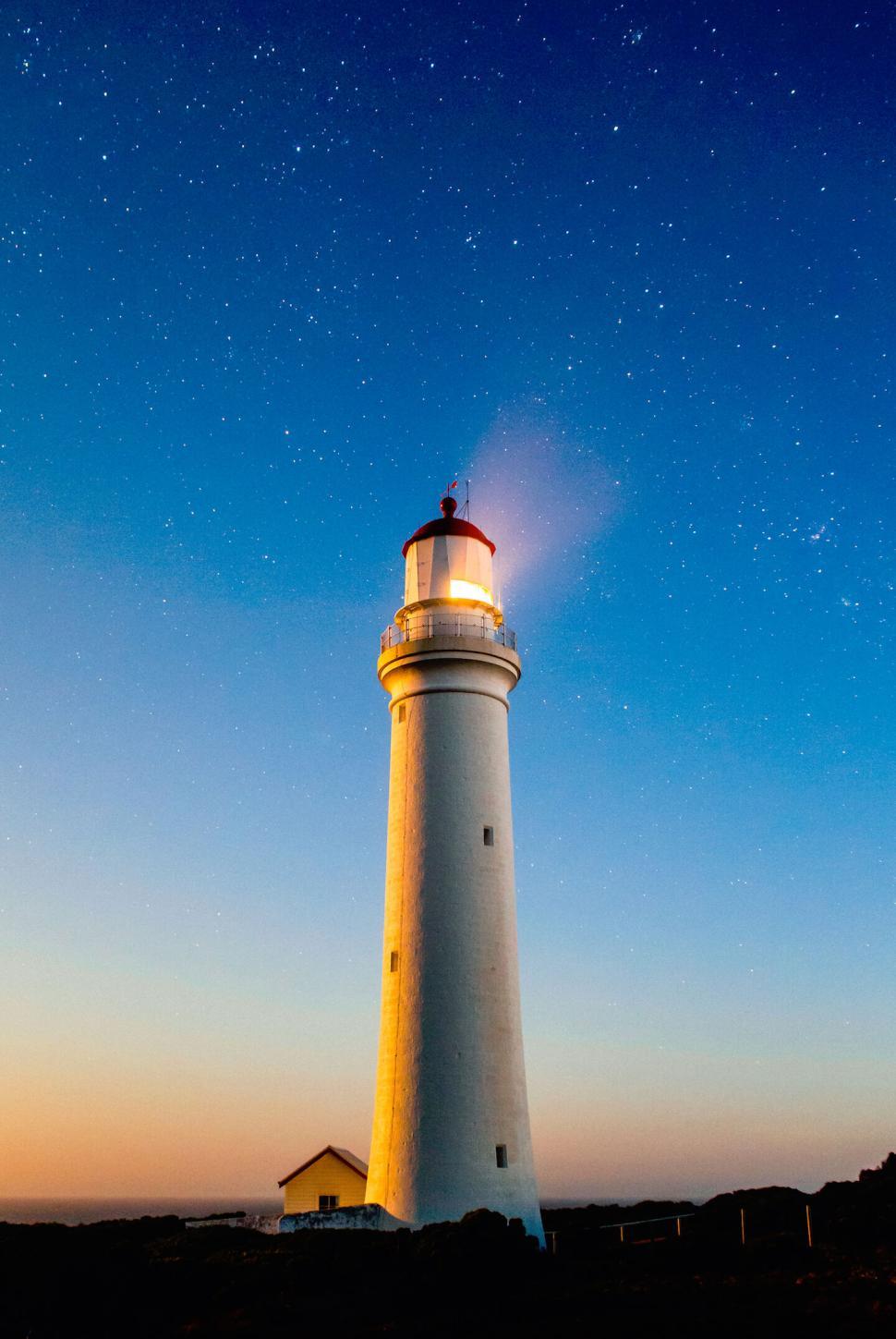 Free Image of Illuminated lighthouse under a starry night sky with clear horizon. 