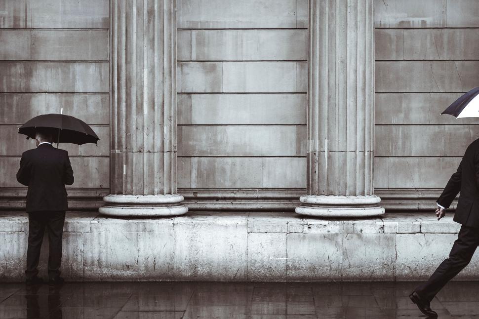 Free Image of Men with umbrellas walking past ancient architectural columns. 