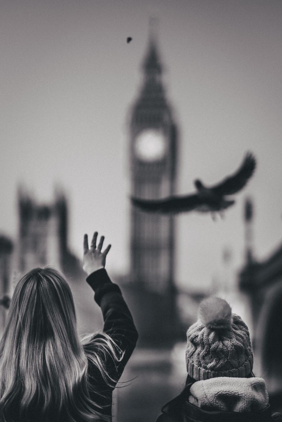 Free Image of Two individuals near Big Ben with a bird flying overhead. 