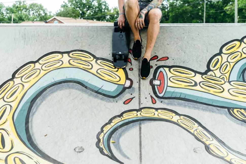Free Image of Person sitting on a skateboard ramp with tentacle graffiti art. 