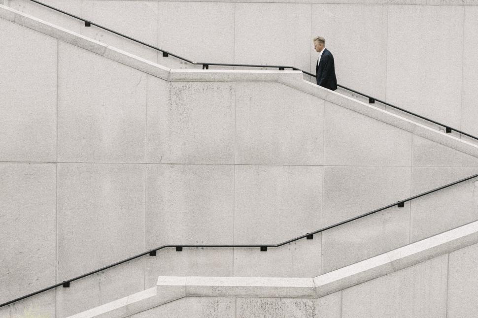 Free Image of Man walking up concrete stairs with a minimalist design background 