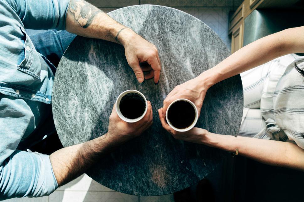 Free Image of Two People Sitting at a Table with Coffee Cups in Hand 