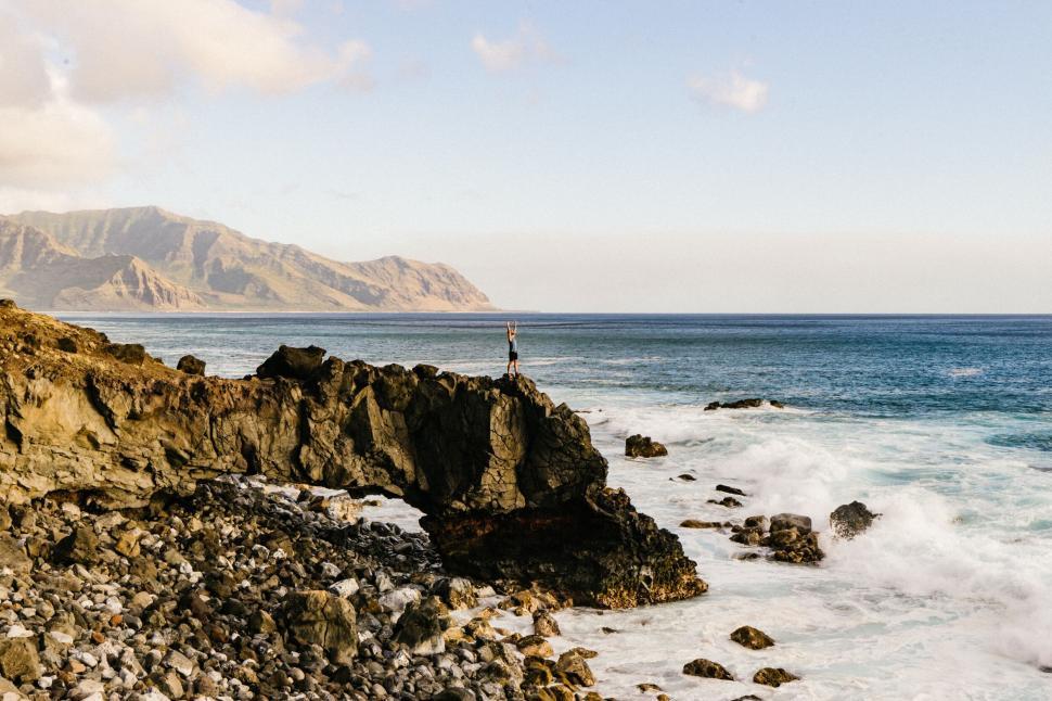 Free Image of Man standing on rocky cliff with ocean waves crashing below him 