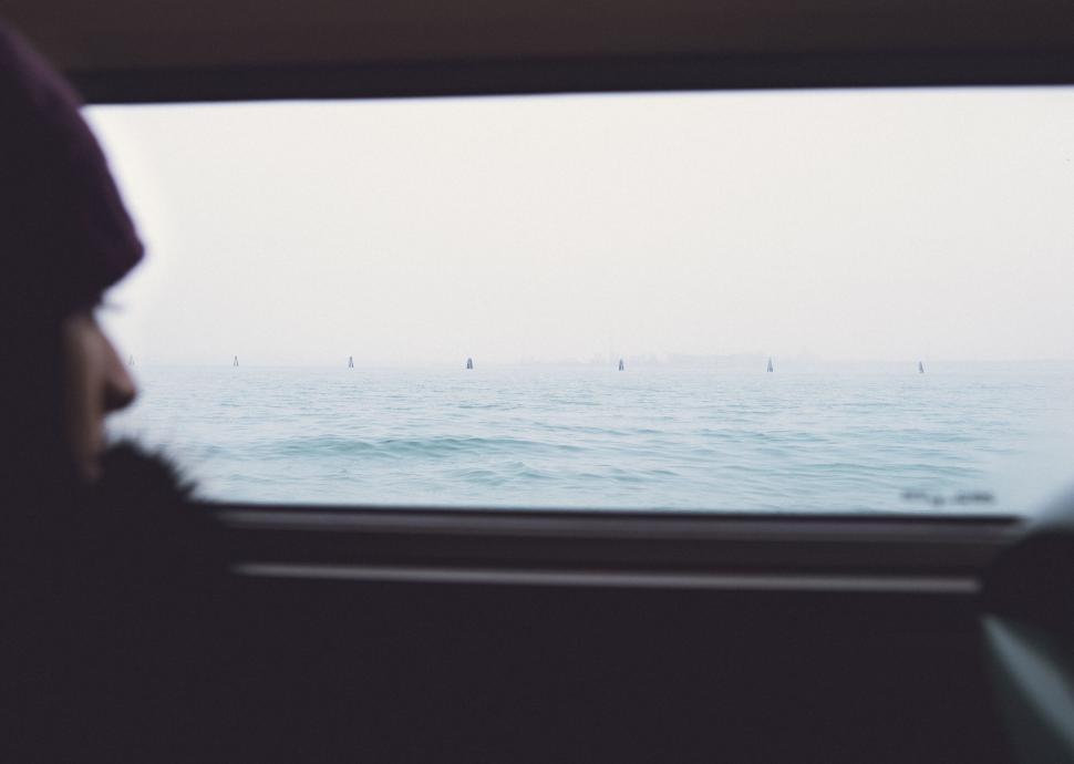 Free Image of Person gazing out of a vehicle window at the calm waters outside 