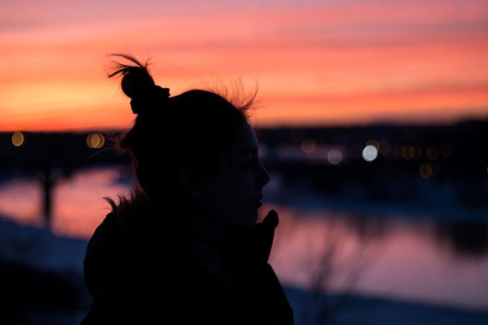 Free Image of Silhouette of woman at sunset overlooking a calm, reflective river. 