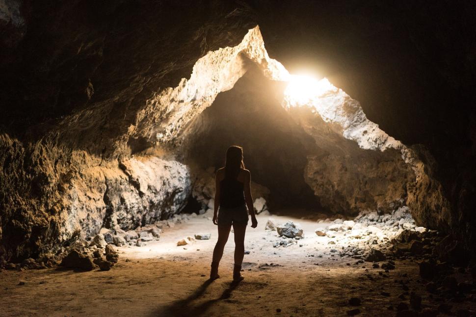 Free Image of Person standing in illuminated cave entrance, surrounded by shadows 