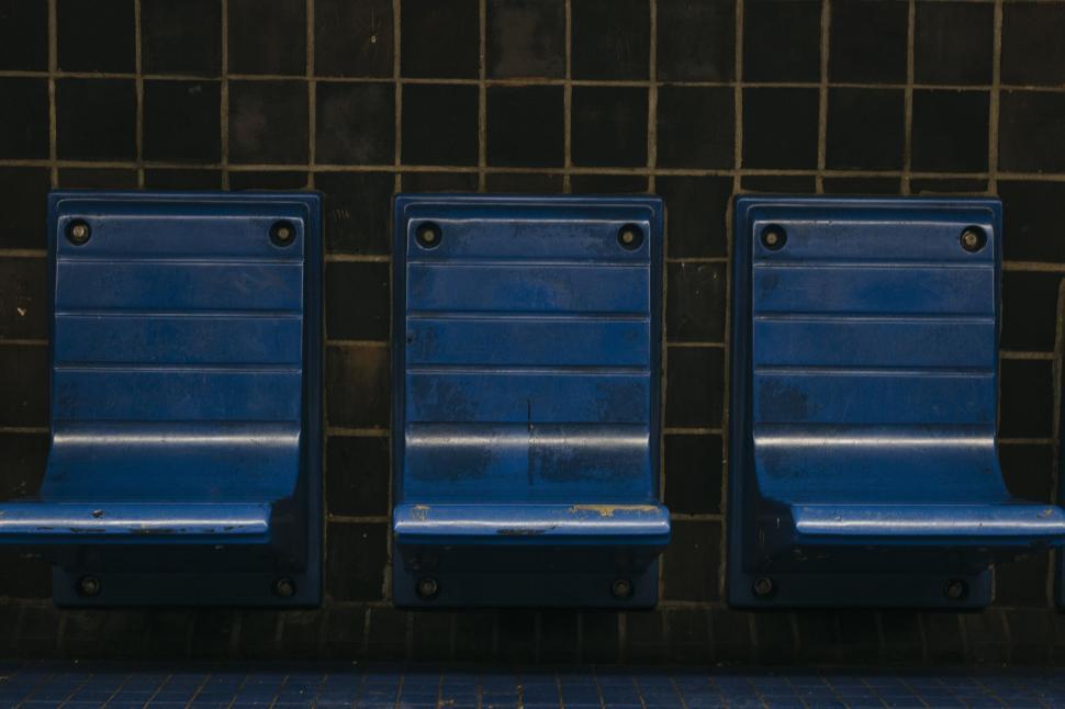 Free Image of Three empty blue chairs against tiled black wall in a waiting area 