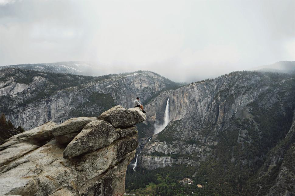 Free Image of Solitary figure on rock ledge overlooking mountainous valley landscape 
