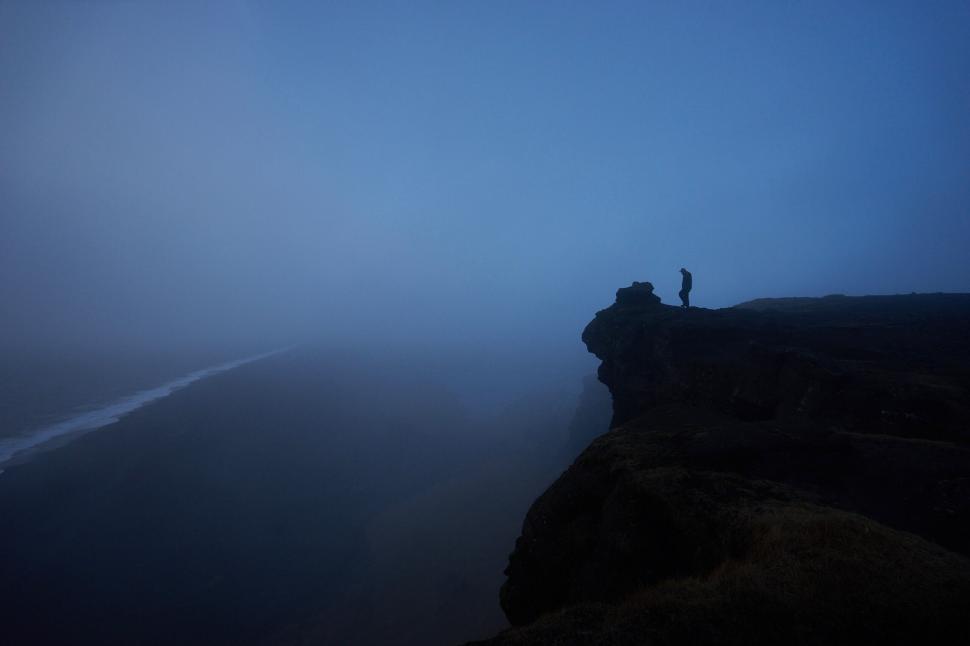 Free Image of Person standing at the edge of a cliff during a foggy dusk 