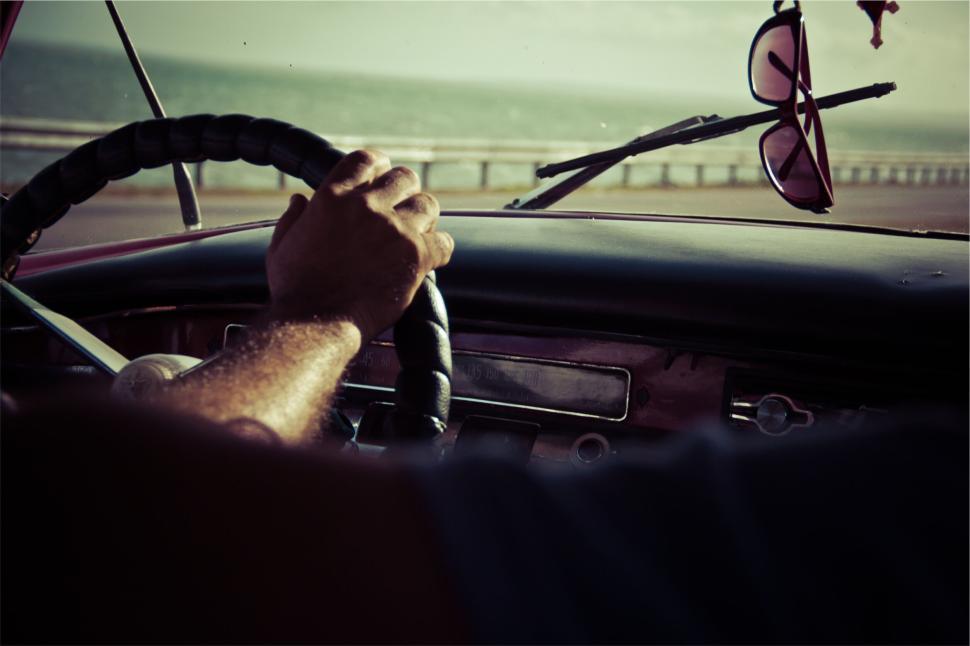 Free Image of Hand on the steering wheel driving a car along a sunny coastline 