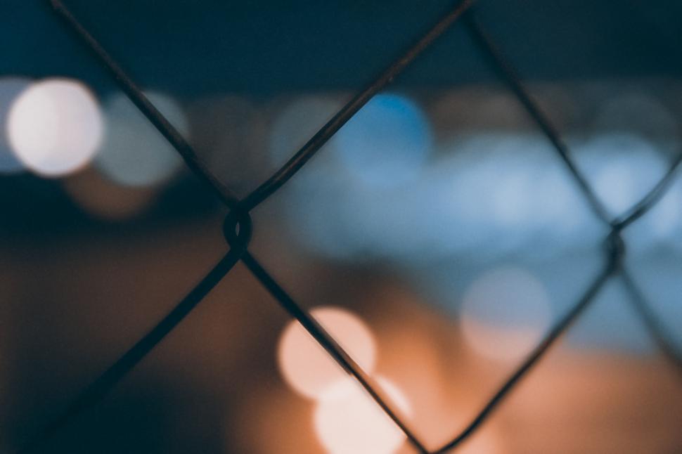 Free Image of Blurred lights behind a chain-link fence at night creating bokeh effect 