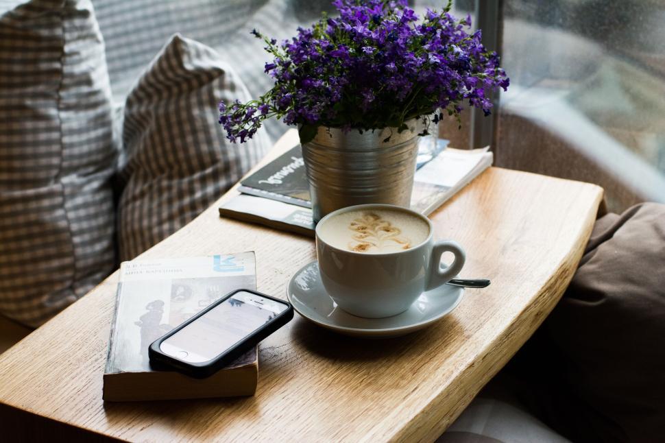 Free Image of Comfortable cafe scene with coffee, book, phone, and flowers 