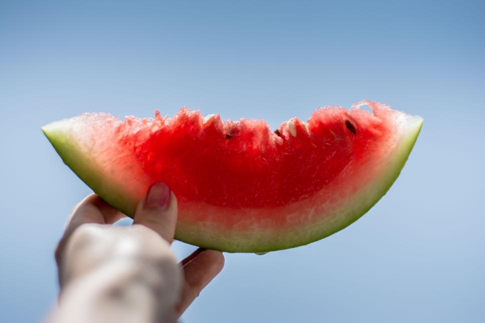 Free Image of Hand holding a juicy slice of watermelon against clear blue sky 