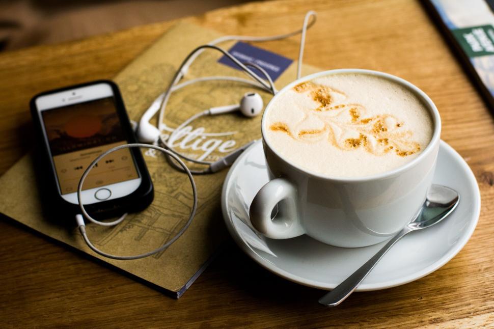Free Image of White cup of cappuccino with sketch alongside earphones and iPhone. 