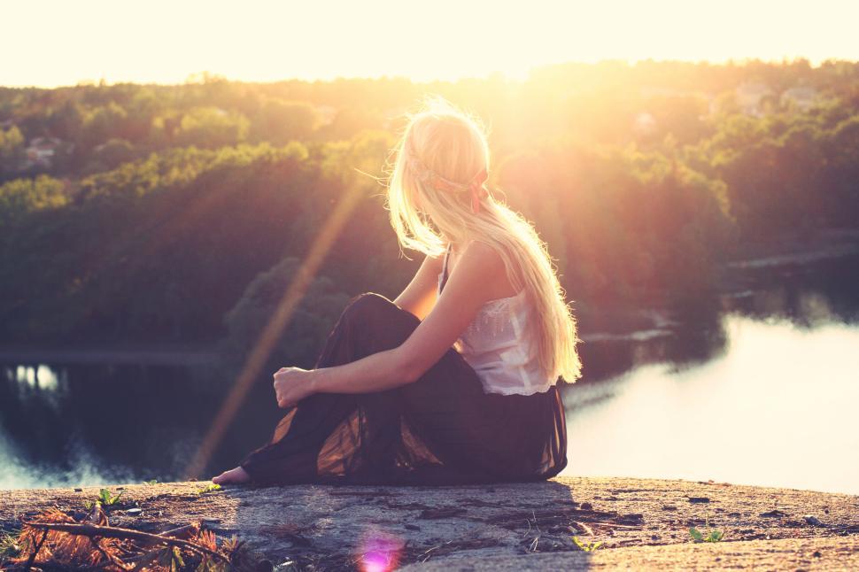 Free Image of Blonde woman on a hilltop overlooking a serene river during sunset. 