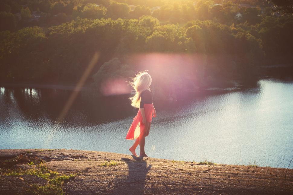 Free Image of Woman standing on edge of hill at sunset in flowing red dress. 