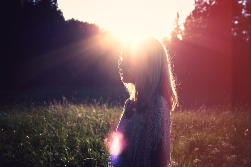 Free Image of Silhouetted woman in field at sunset with lens flare and sun rays 
