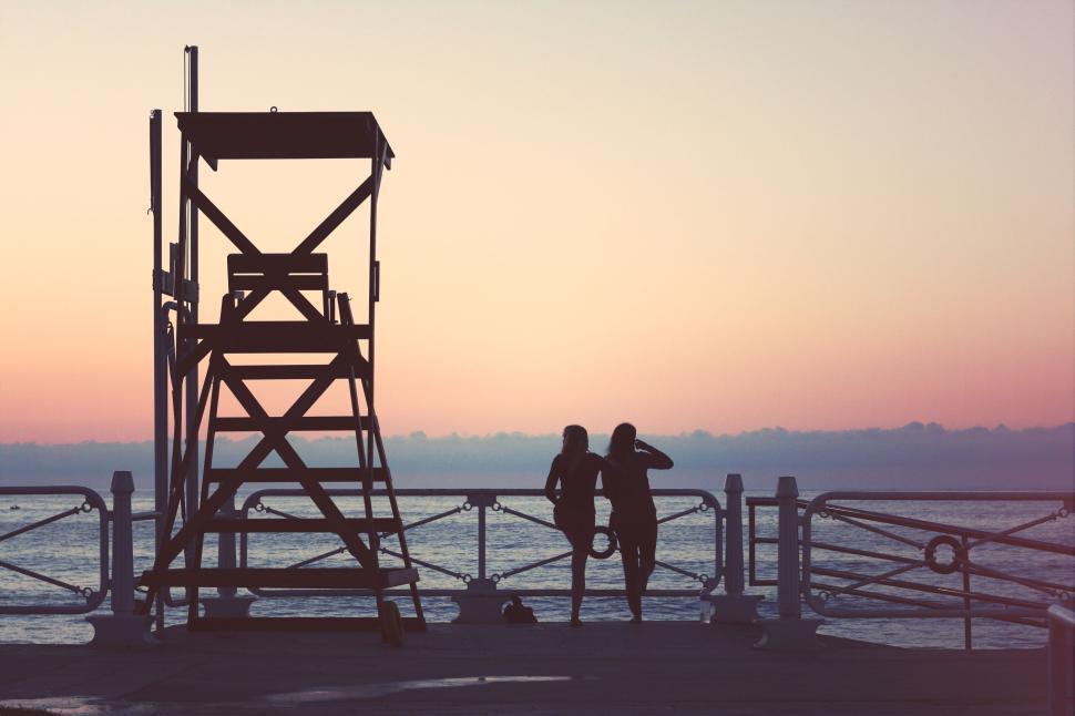 Free Image of Two people silhouetted, leaning on railing by the sea at twilight 
