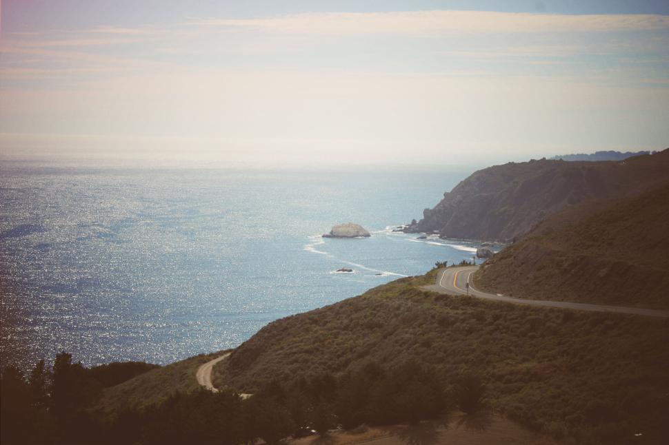 Free Image of A scenic coastal view with winding road and distant boulder. 