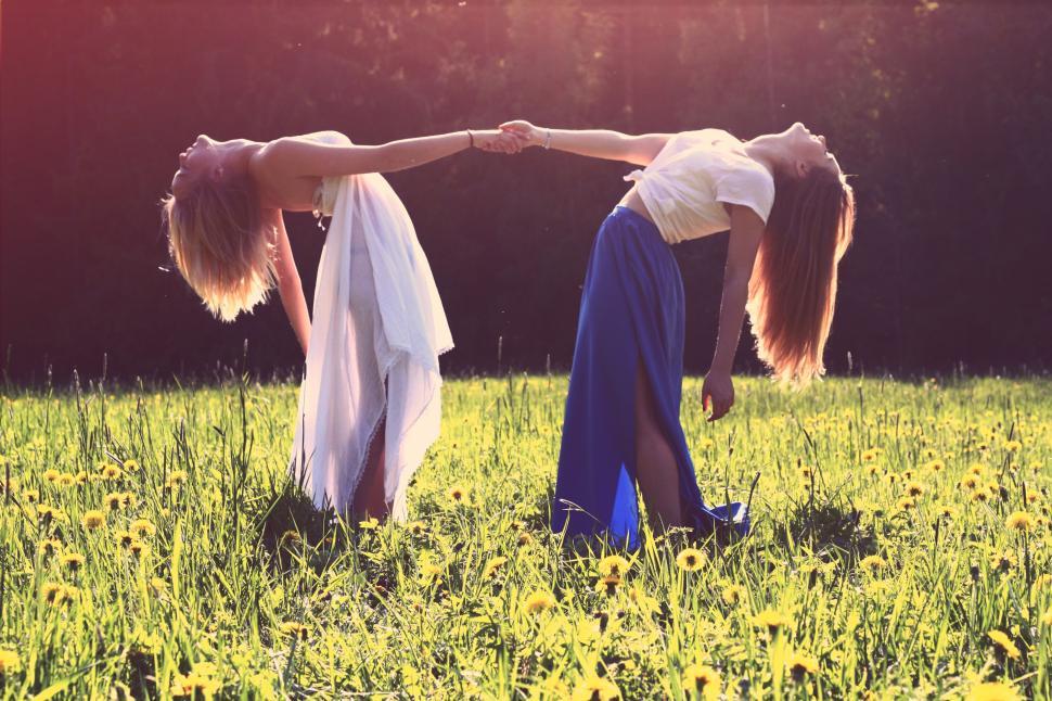 Free Image of Two girls holding hands and bending backwards in yellow field. 