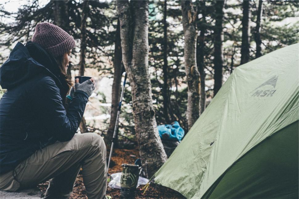 Free Image of Camper enjoys hot drink by tent in winter forest after long hike 