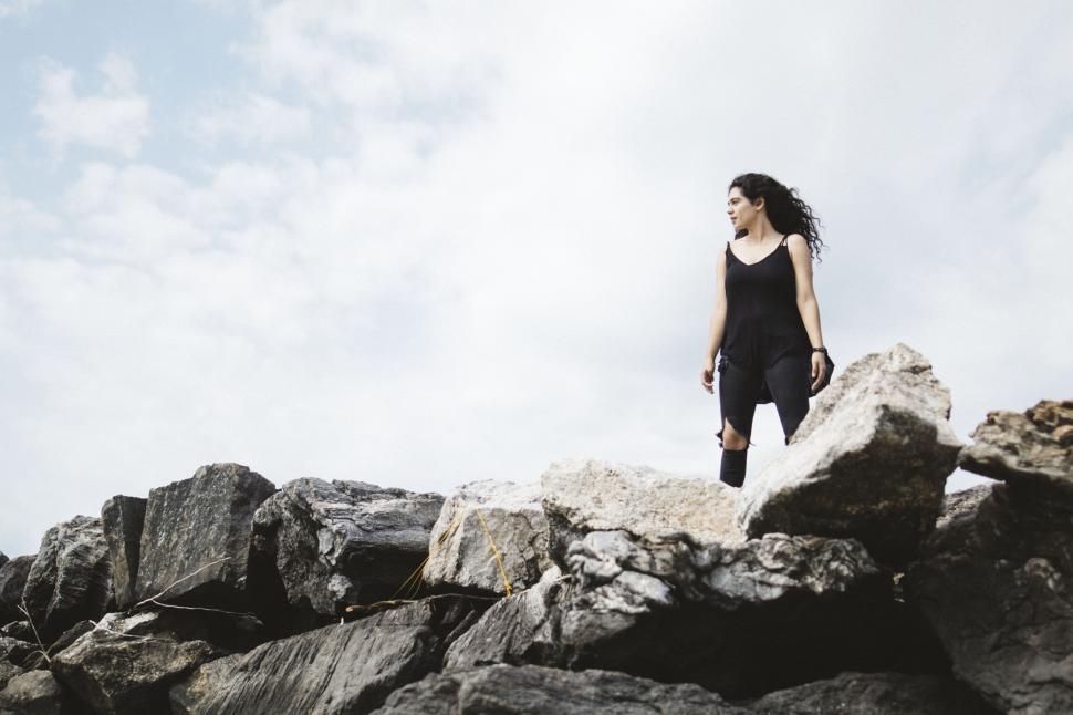 Free Image of Person standing confidently on rocky outcrop under a cloudy sky. 