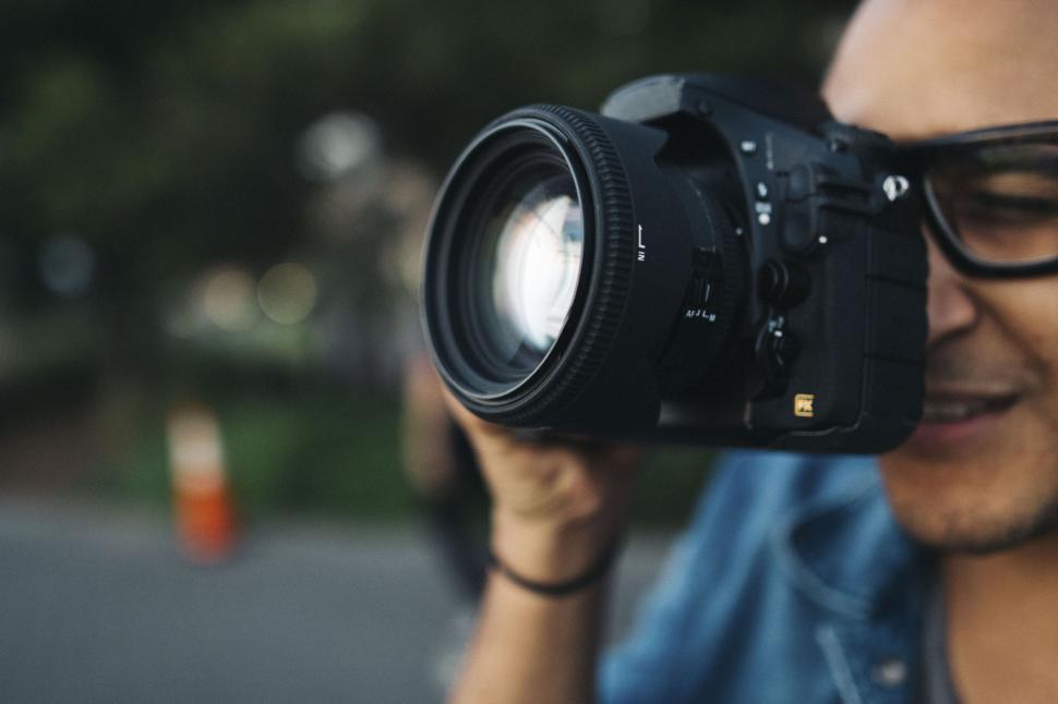 Free Image of Photographer holding camera ready to take a shot, blurred background. 