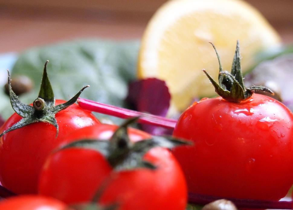 Free Image of Close-up of fresh red tomatoes with a slice of lemon in the background. 